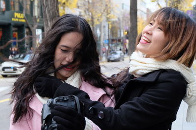 Cheerful young woman embracing friend in city