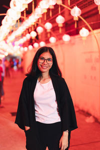 Portrait of smiling young woman standing against illuminated lanterns at night