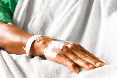 Cropped hand of woman with iv drip lying on bed in hospital