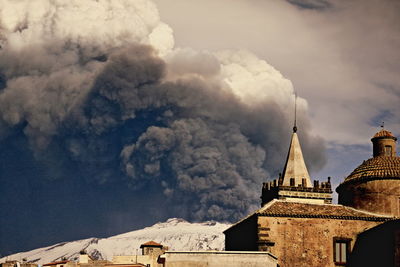 Houses against snowcapped mt etna emitting smoke