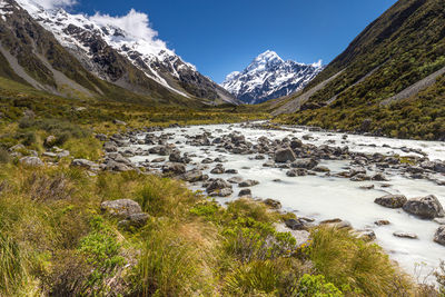 Scenic view of stream by snowcapped mountains against sky