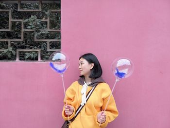 Smiling young woman holding balloon against wall