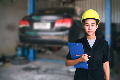 Portrait of smiling female mechanic holding clipboard at garage