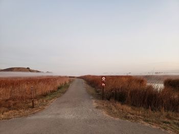 Empty road amidst field against sky