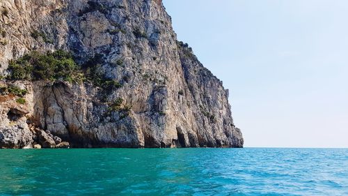 Rock formations by sea against clear sky