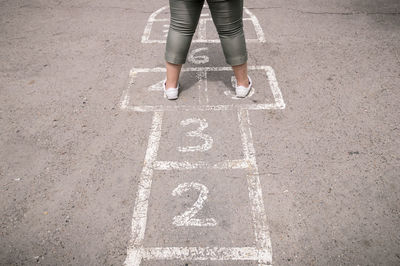 Low section of girl playing hopscotch on road