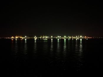 Illuminated cityscape by sea against sky at night