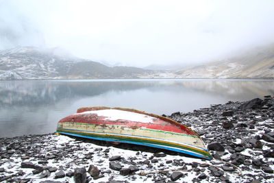 Upside down boat moored by river against mountains during foggy weather