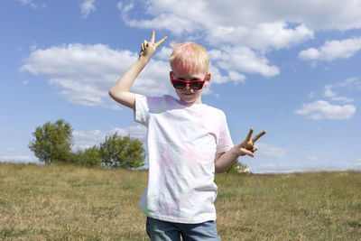 Little blonde boy with colorful paint, powder on clothes posing on holi color festival in meadow