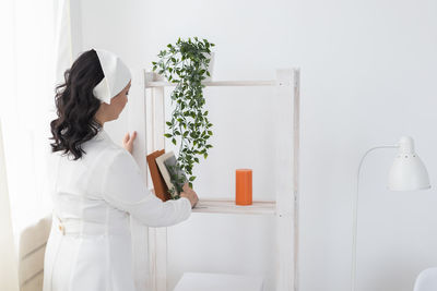 Side view of young woman standing against white wall