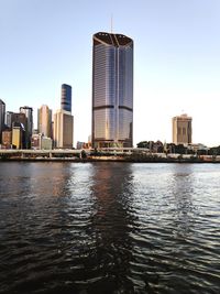 Modern buildings by river against clear sky