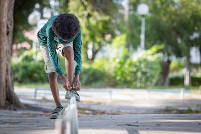 An african black curly haired boy bends down to tie his shoelaces.