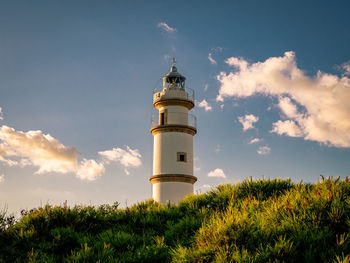 Lighthouse on field by building against sky