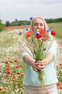Beautiful middle-aged blonde woman stands among a flowering field of poppies