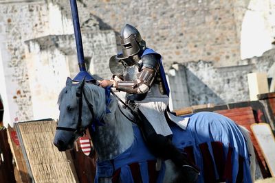 Man wearing warrior costume sitting on horse against wall