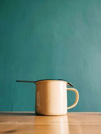 A cup made of tin, with a spoon on top, which is placed on a wooden table