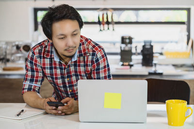 Portrait of young woman using laptop while standing in cafe