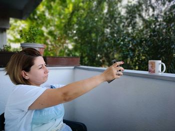 Side view of mature woman taking selfie with smart phone while sitting in balcony