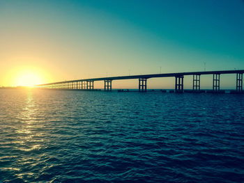 Bridge over sea against clear sky during sunset