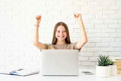 Smiling young woman using laptop on table against wall