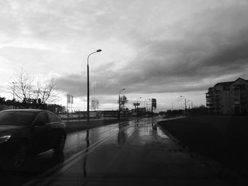 Road passing through city against cloudy sky