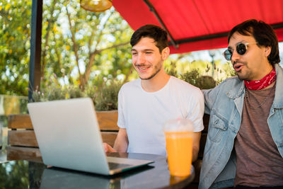 Smiling young men looking at laptop while sitting at cafe