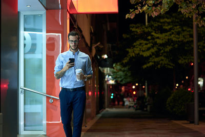 Young businessman walks with his smartphone and coffee cup at ni