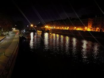 Illuminated bridge over river against sky in city at night