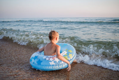 Rear view of shirtless boy at beach against sky