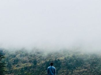 Rear view of man looking at mountain during foggy weather