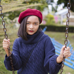 Portrait of young woman holding swing at playground