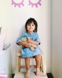 Portrait of cute baby girl with toy sitting on table against wall at home