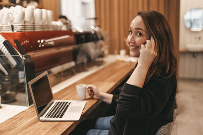 Young woman using phone while sitting on table