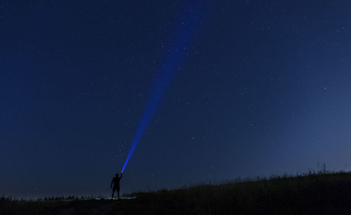 Silhouette man projecting flashlight in sky at night