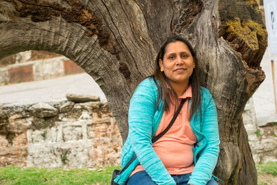 Portrait of smiling woman against tree trunk