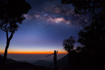 Silhouette man by trees against sky at night