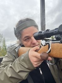 A portrait of a woman aiming with a rifle in the forest on an autumn day.