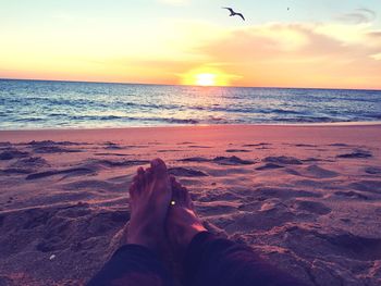 Low section of woman on beach against sky during sunset