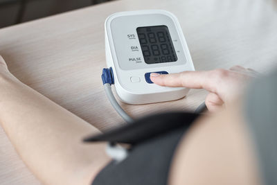 Midsection of woman measuring blood pressure with gauge on table