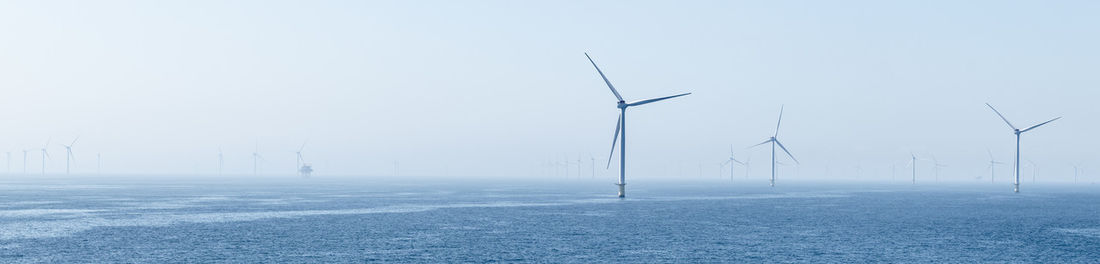 A cluster of turbines of a wind farm on the blue glittering sea under a cloudless blue sky