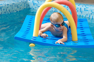 Toddler child crawling through tunnel on the water. equipment and toys in swimming pool in goggles. 