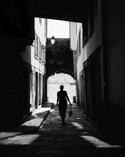 Rear view of man walking on alley amidst buildings in city