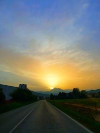 Road by trees against sky during sunset