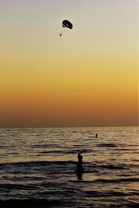 Silhouette people on sea against sky during sunset