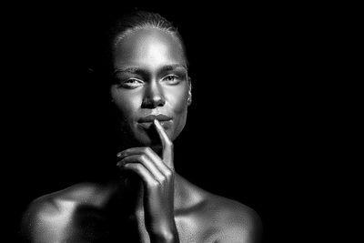 Portrait of young woman with body paint standing against black background