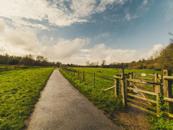 Dirt road amidst field against sky