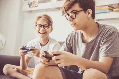 Boys playing video game while holding remote control on sofa