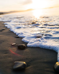 Close-up of frozen water on beach against sky during sunset