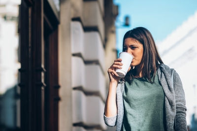 Young woman drinking coffee while looking away in city