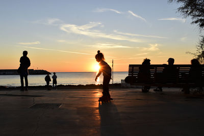 Silhouette people on beach against sky during sunset